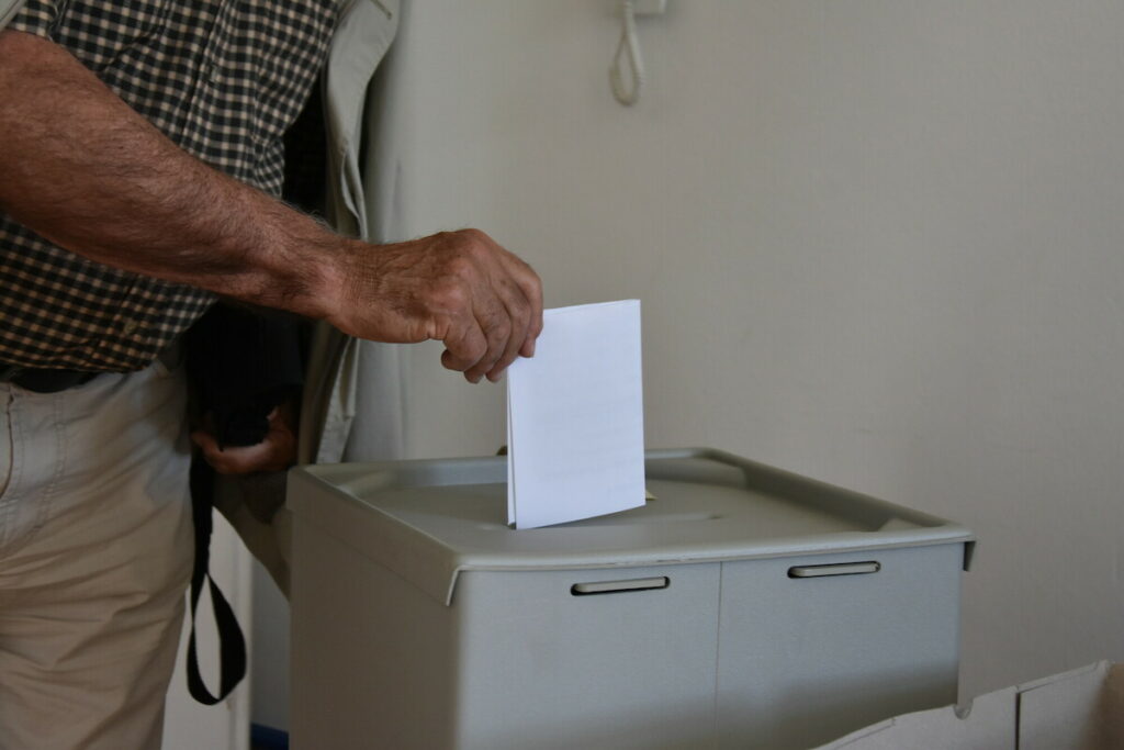 Wahlurne, in die ein Stimmzettel geworfen wird.