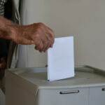 Wahlurne, in die ein Stimmzettel geworfen wird.